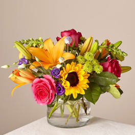 Mixed bouquet of roses, lilies, and a sunflower in a glass vase