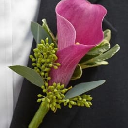 Pink calla lily boutonniere with green accents on a dark suit