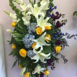 Tall floral spray with white lilies, yellow roses, blue hydrangeas, and purple accents