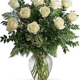White roses arranged in a clear glass vase with dense greenery
