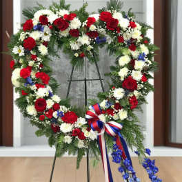 Heart-shaped floral wreath with red, white, and blue flowers on a stand