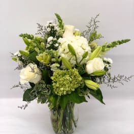Tall arrangement of white and green roses, lilies, hydrangeas, and snapdragons in a clear glass vase.