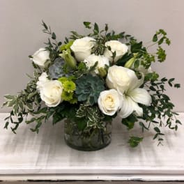 White roses and lilies in a glass vase with green succulents and foliage