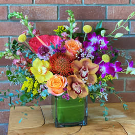 Colorful mixed tropical and garden flower arrangement in a rectangular glass vase