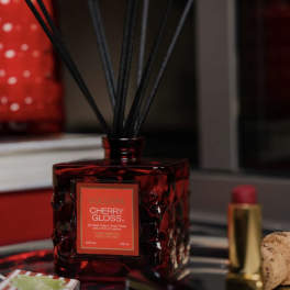 Red reed diffuser bottle with black sticks and a cherry gloss label
