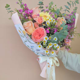 Hand-tied bouquet of peach and pink roses with small white daisies