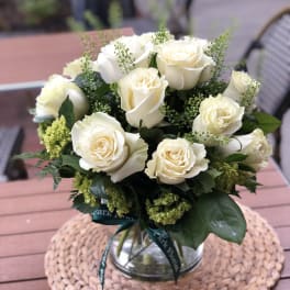 Round bouquet of white roses with green accents in a clear glass vase.