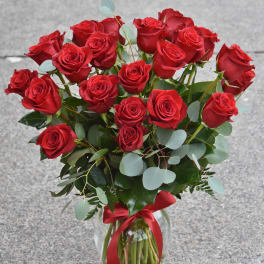 Tall arrangement of long-stem red roses in a clear glass vase with a red ribbon bow