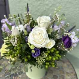 Arrangement of white roses and purple flowers in a light green vase on a mosaic table