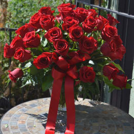 Large bouquet of red roses in a clear vase with a red ribbon bow on a mosaic table