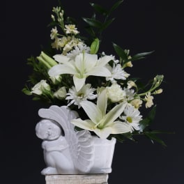 White lilies and daisies arranged in a white ceramic planter