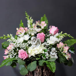 Pink and white floral arrangement with angel figurines in a vase