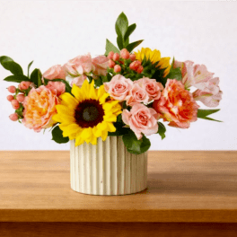 Mixed bouquet with sunflowers, pink roses, and carnations in a ribbed vase