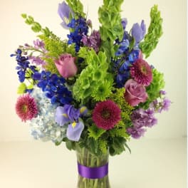 Mixed bouquet of purple, blue, and green flowers in a glass vase