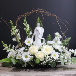 White floral arrangement with roses and daisies around a figurine