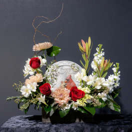 Sympathy floral arrangement with red roses and white blooms around a memorial plaque