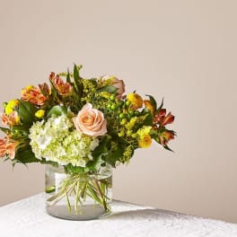 Mixed bouquet of peach roses, white hydrangea, and yellow flowers in a glass vase