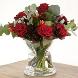 Arrangement of red roses with dark accent blooms and eucalyptus in a clear glass vase