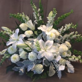 Large all-white floral arrangement with lilies, roses, and mums with green accents in a fan shape