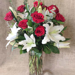 Tall arrangement of red roses and white lilies in a clear glass cylinder vase