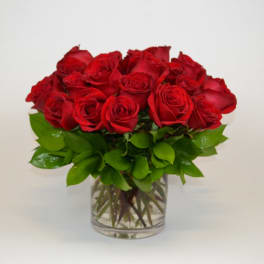 Short arrangement of red roses in a clear glass vase with a compact, rounded shape.