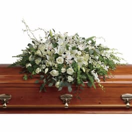 White casket spray of lilies, roses, and orchids on a polished wood casket
