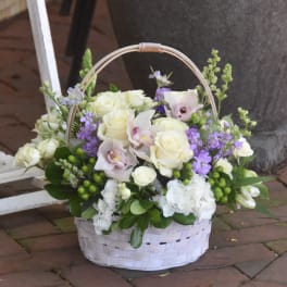 White basket of ivory roses, orchids, and purple flowers with green berries