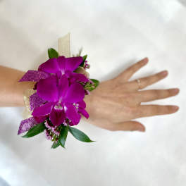 Wrist corsage with bright purple orchids, ribbon, and small blooms on a person's hand