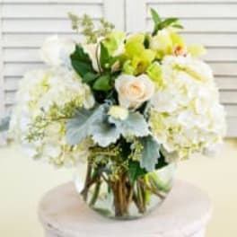 Round arrangement of white hydrangeas, pale roses, and green orchids in a clear glass vase