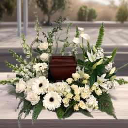 White floral funeral arrangement surrounding a wooden urn