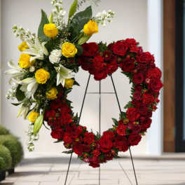 Heart-shaped floral wreath on a stand with red and yellow roses and white lilies