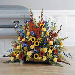 Large funeral basket of red, yellow, and blue flowers in front of a silver casket