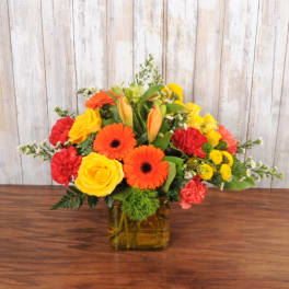 Bright mix of orange, yellow, and red flowers in a yellow glass cube vase