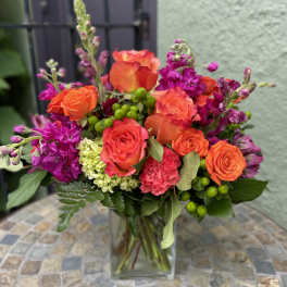 Bright arrangement of orange roses and pink flowers in a clear glass vase on a mosaic table