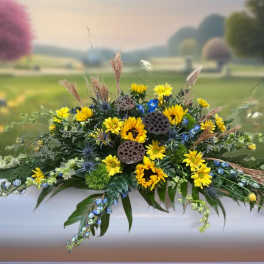 Yellow and blue floral casket spray with greenery and dried accents
