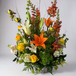 Tall floral arrangement with orange lilies, yellow roses, and white blooms in a basket