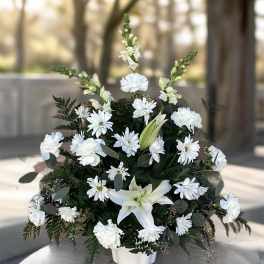 White flowers arranged in a low white vase with dark greenery.