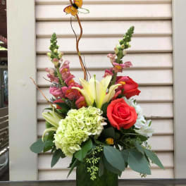 Mixed floral arrangement in a green vase with roses, lilies, and hydrangea