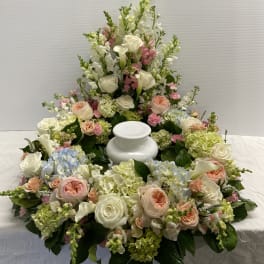 Large white and pastel floral funeral arrangement around a white urn