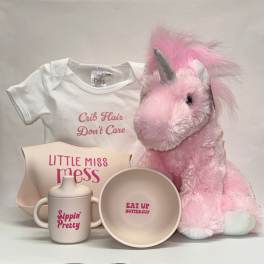 Pink plush unicorn with baby onesie, bib, bowl, and sippy cup in cream and pink tones
