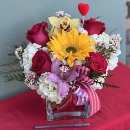 Bouquet of red roses, a yellow sunflower, and pink orchids in a glass vase