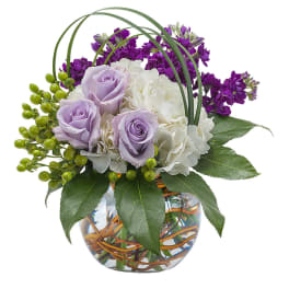 Lavender roses and white flowers in a glass vase with purple blooms