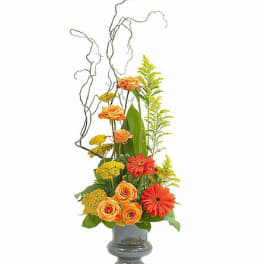 Orange roses and gerbera daisies in a gray vase with tall curly branches