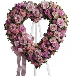 Heart-shaped pink floral wreath on a stand with a ribbon bow