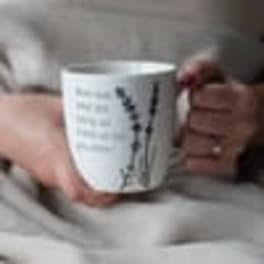 Person holding a white ceramic mug with a black floral design