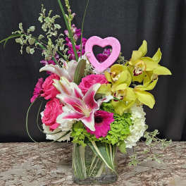 Bright mixed bouquet in a clear glass vase with a pink heart pick