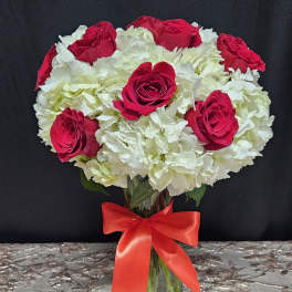 Red roses and white hydrangeas in a glass vase with a red ribbon