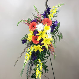 Tall standing floral spray with yellow lilies, orange gerberas, white blooms, and purple flowers