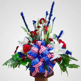 Red, white, and blue floral arrangement with a patriotic ribbon bow