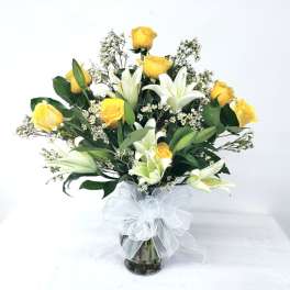 Yellow roses and white lilies in a glass vase with a white bow